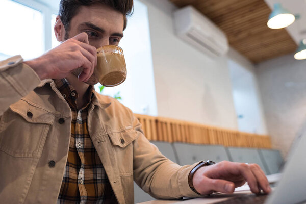 Freelancer drinking coffee and using laptop in cafe