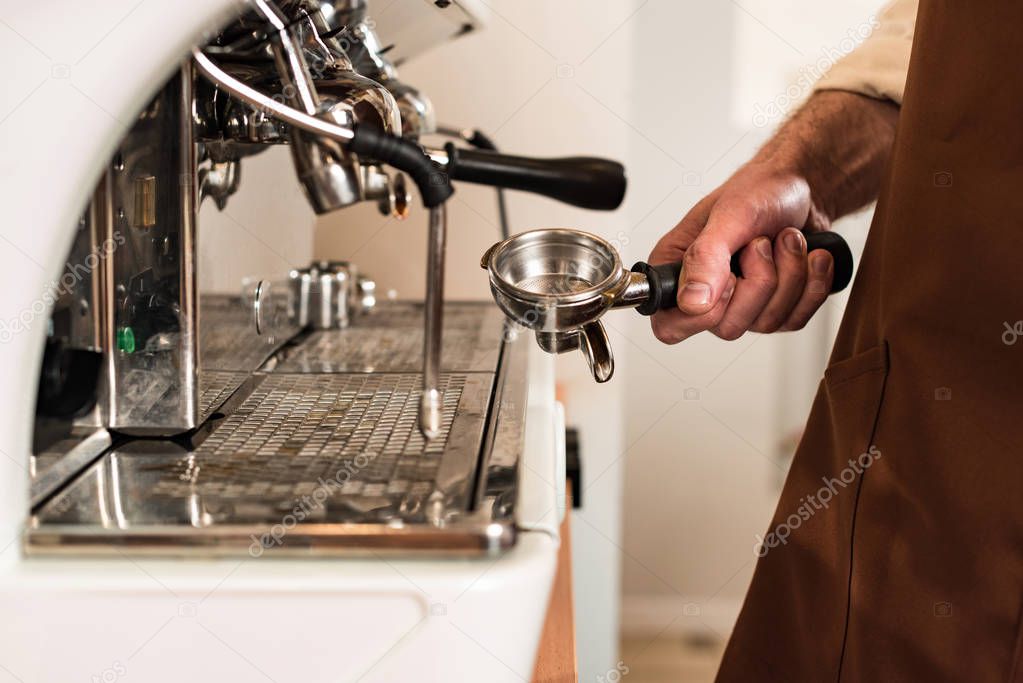 Partial view of barista holding portafilter near coffee machine