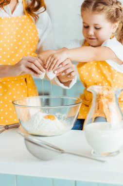 anne ve kızı mutfakta birlikte pişirirken kasede un ezilmiş yumurta ekleyerek