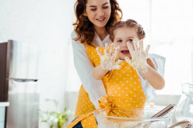 gülümseyen anne seçici odak elleri üzerinde hamur ile heyecanlı kızı bakıyor 