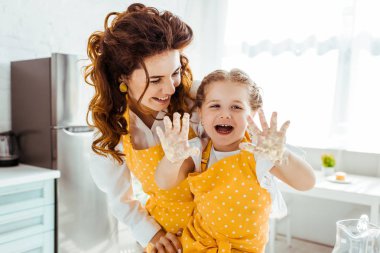 smiling mother looking at laughing happy daughter with dirty hands in dough clipart