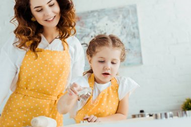 sarı polka nokta önlük mutlu anne hamur kalıpları kullanarak kızı bakıyor 