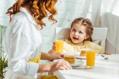 anne ile kahvaltı yaparken portakal suyu ile cam tutan sevimli mutlu çocuk seçici odak