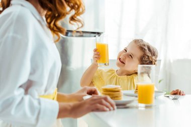 duygusal mutlu kızı seçici odak anne bakarak ve kahvaltı yaparken portakal suyu ile cam tutarak