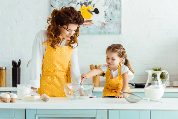 母亲在波尔卡点黄色围裙看着可爱的女儿与气球在厨房的胡须 — 图库照片