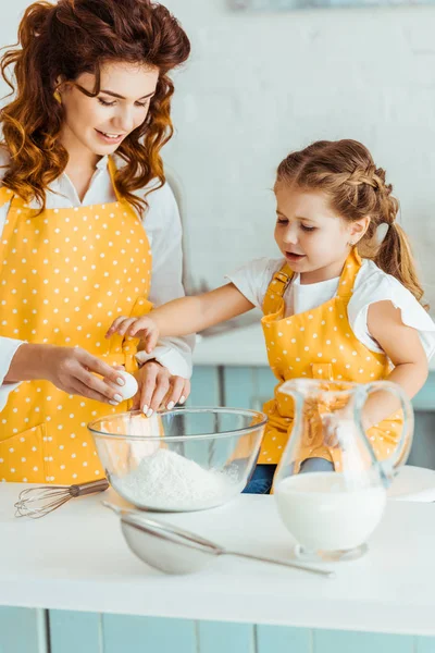 台所で娘と一緒に料理しながら ボウルに小麦粉に卵を加える笑顔の母 — ストック写真