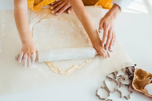 top view of mother and daughter rolling out dough near dough molds on table