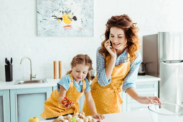 Mãe Feliz Falando Smartphone Enquanto Filha Segurando Tomates Cereja — Fotografia de Stock