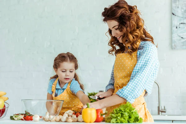 Mama Zâmbitoare Tăiere Legume Proaspete Crude Lângă Fiica Bucătărie — Fotografie, imagine de stoc