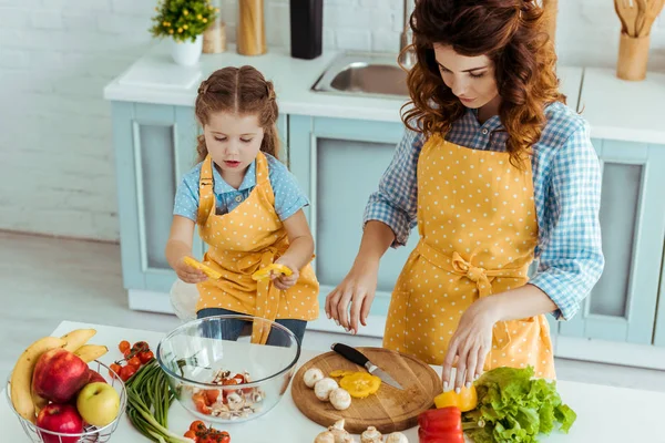 Mãe Cortando Vegetais Crus Frescos Enquanto Filha Colocando Fatias Tigela — Fotografia de Stock