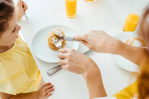 Vista Recortada Madre Cortando Panqueques Con Tenedor Cuchillo Cerca Hija — Foto de Stock