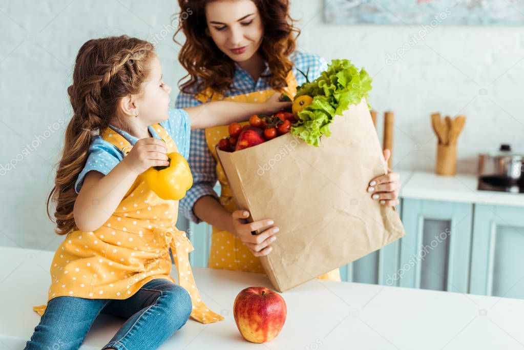 daughter taking apple and bell pepper out of  paper bag in kitchen