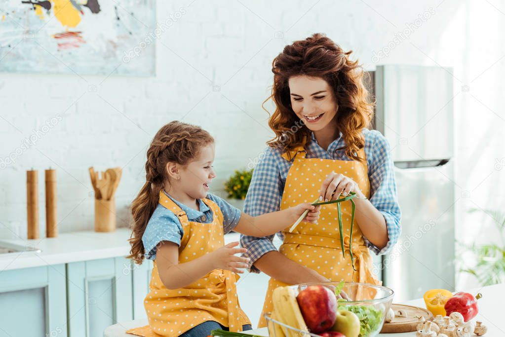 cute daughter in polka dot yellow apron giving mother green onions