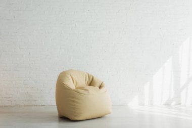 modern evde tuğla duvara yakın bej fasulye çanta sandalye yakınında güneş ışığı 