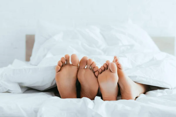 cropped view of boyfriend and girlfriend with barefoot lying in bed