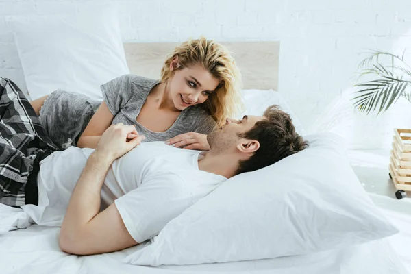 开朗的金发女孩看着男朋友躺在枕头上在卧室 — 图库照片