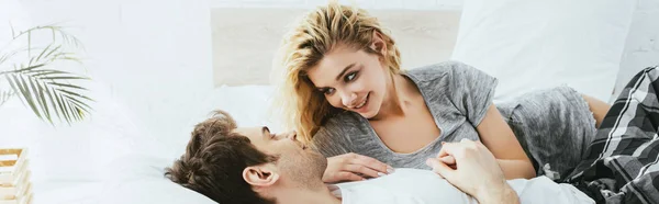 全景拍摄的欢快的金发女孩看着男朋友躺在枕头上在卧室 — 图库照片