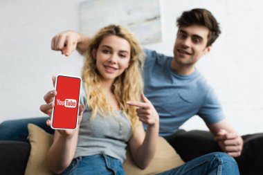 ekranda youtube uygulaması ile akıllı telefon parmakları ile işaret neşeli adam ve sarışın kadın seçici odak