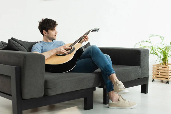 Hombre Guapo Sentado Sofá Tocando Guitarra Acústica Casa — Foto de Stock