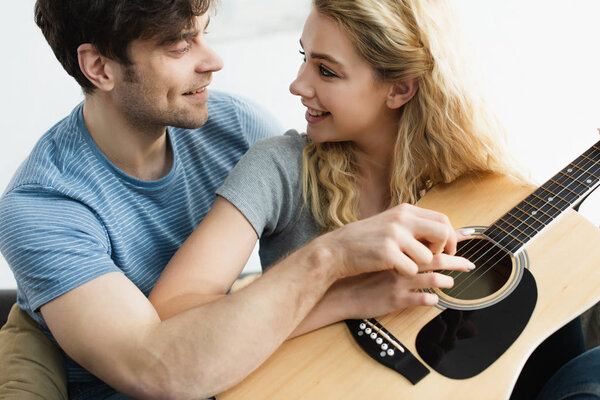 happy man and cheerful blonde woman holding hands of strings and looking at each other 