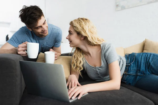 Happy Handsome Man Holding Cups Blonde Girl Using Laptop — Stock Photo, Image