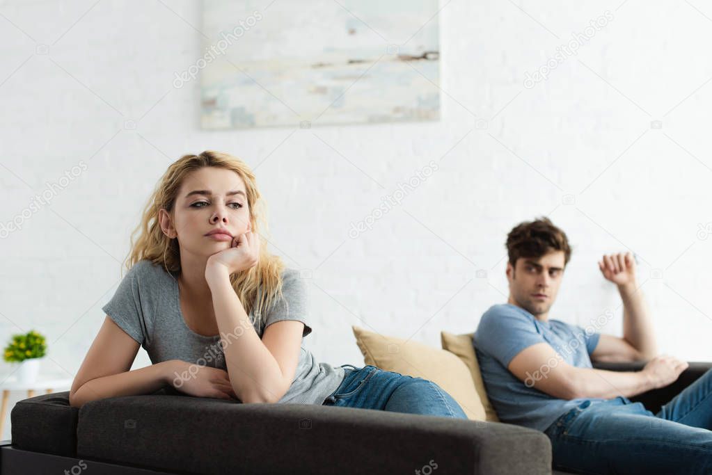 selective focus of upset blonde woman sitting on sofa near man after quarrel 