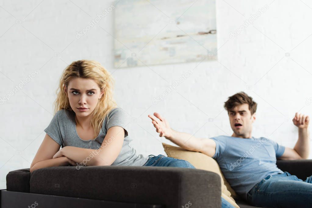 selective focus of frustrated blonde woman with crossed arms near man gesturing in living room 