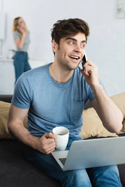 Dizüstü Bilgisayarın Yakınındaki Akıllı Telefonda Konuşan Bardak Tutan Neşeli Adam — Stok fotoğraf