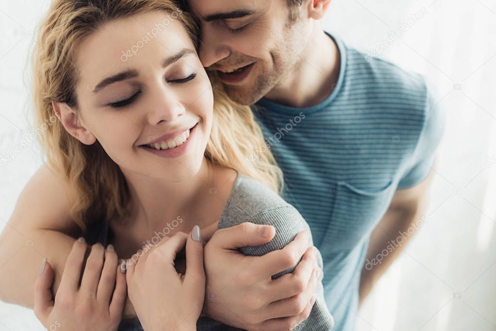 cheerful and handsome man hugging young happy woman with closed eyes