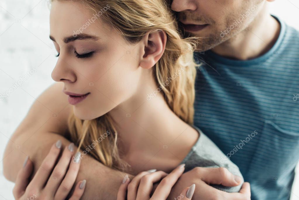 cropped view of man hugging beautiful blonde girl with closed eyes