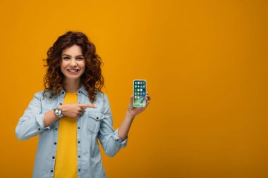 turuncu üzerinde iphone parmak ile işaret neşeli kıvırcık kızıl kadın 