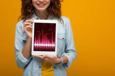 turuncu izole ekranda grafikler ve grafikler ile dijital tablet tutan neşeli kıvırcık kız kırpılmış görünümü 