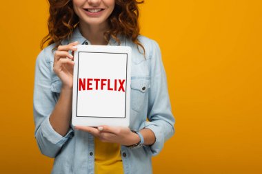turuncu izole ekranda netflix uygulaması ile dijital tablet tutan neşeli kıvırcık kız kırpılmış görünümü 