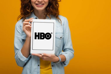 turuncu izole ekranda hbo uygulaması ile dijital tablet tutan neşeli kıvırcık kız kırpılmış görünümü 
