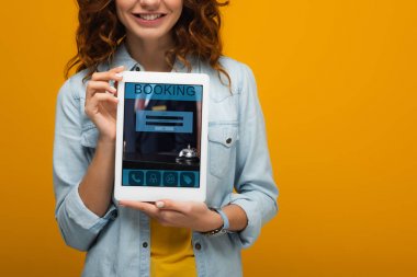 turuncu izole ekranda rezervasyon uygulaması ile dijital tablet tutan neşeli kıvırcık kız kırpılmış görünümü 