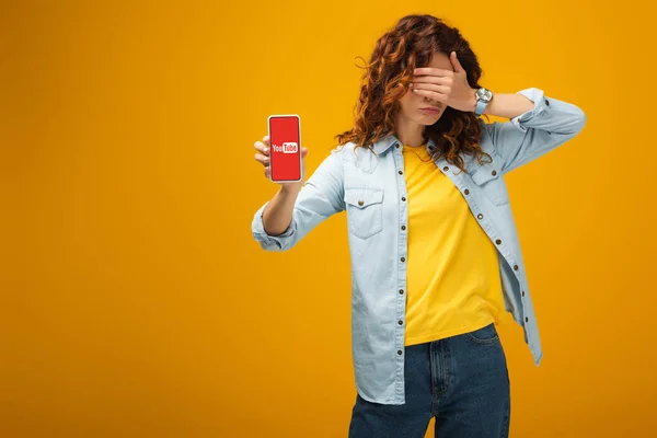 Mulher Ruiva Encaracolado Cobrindo Olhos Segurando Smartphone Com Aplicativo Youtube — Fotografia de Stock