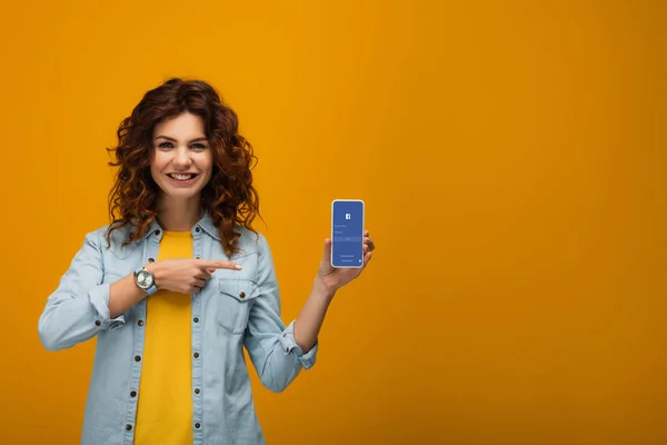 Cheerful Curly Redhead Woman Pointing Finger Smartphone Facebook App Screen — Stock Photo, Image