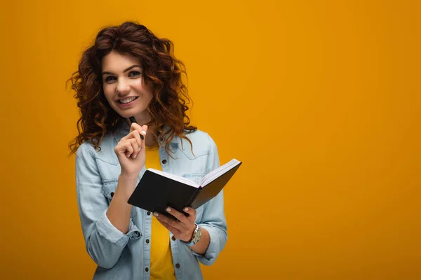 Sonriente Pelirroja Joven Sosteniendo Cuaderno Pluma Naranja — Foto de Stock