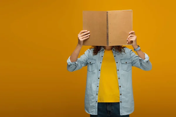 オレンジのノートで顔を覆っている若い女性は — ストック写真
