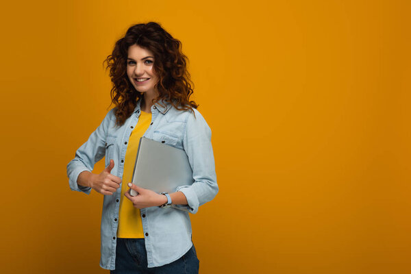 веселая рыжая девушка держит ноутбук и показывает большой палец на оранжевый
 