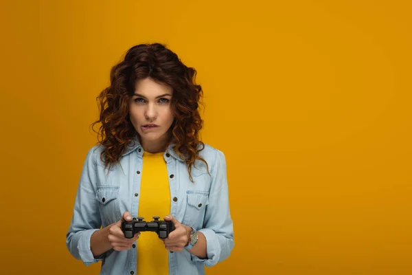 Curly Redhead Woman Biting Lips While Playing Video Game Orange — Stock Photo, Image