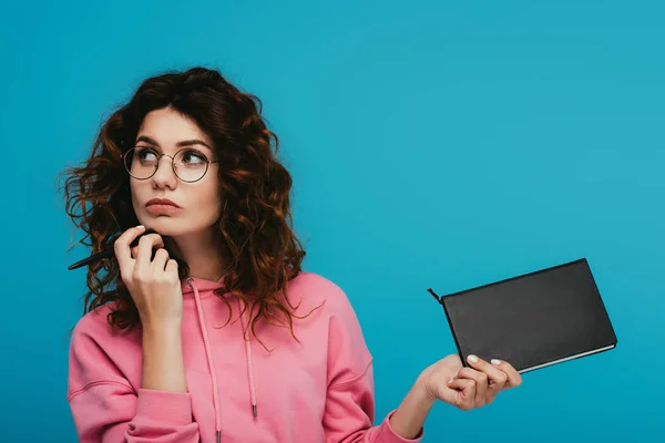 Pensive Curly Girl Glasses Holding Notebook Pen Isolated Blue — Stock Photo, Image