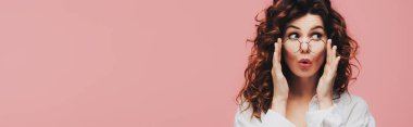 panoramic shot of surprised curly girl touching glasses isolated on pink clipart