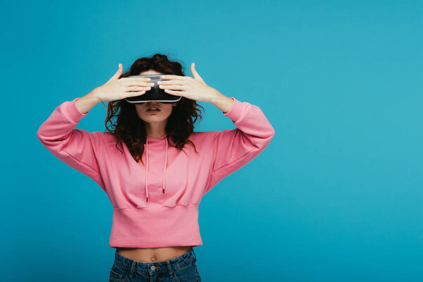 curly girl wearing virtual reality headset while covering eyes on blue 