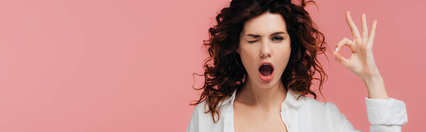 panoramic shot of curly young woman with red hair showing ok sign isolated on pink