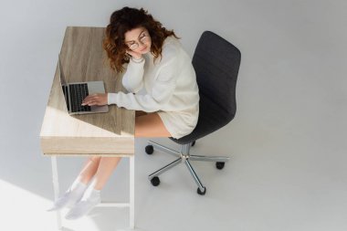 gri dizüstü bilgisayarın yanında oturan kıvırcık kızıl saçlı kızın havai görünümü 