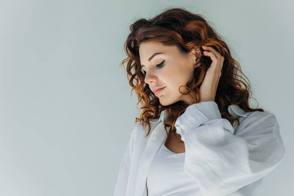 attractive curly young woman touching hair on grey 