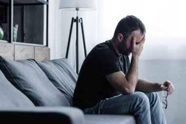 depresif adam kanepede otururken gözlük tutan ve el ile yüz kaplama