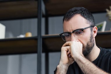 gözlüklü düşünceli sakallı adam yüzüne yakın el ele tutuşuyor ve aşağı bakıyor