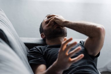 depressed man suffering while lying on sofa and holding hand on face